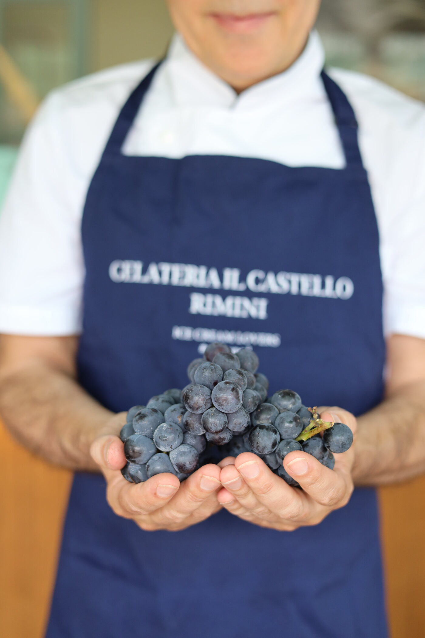 Le mani di Marco Ottaviani con dell'uva, davanti al grembiule Gelateria Il Castello